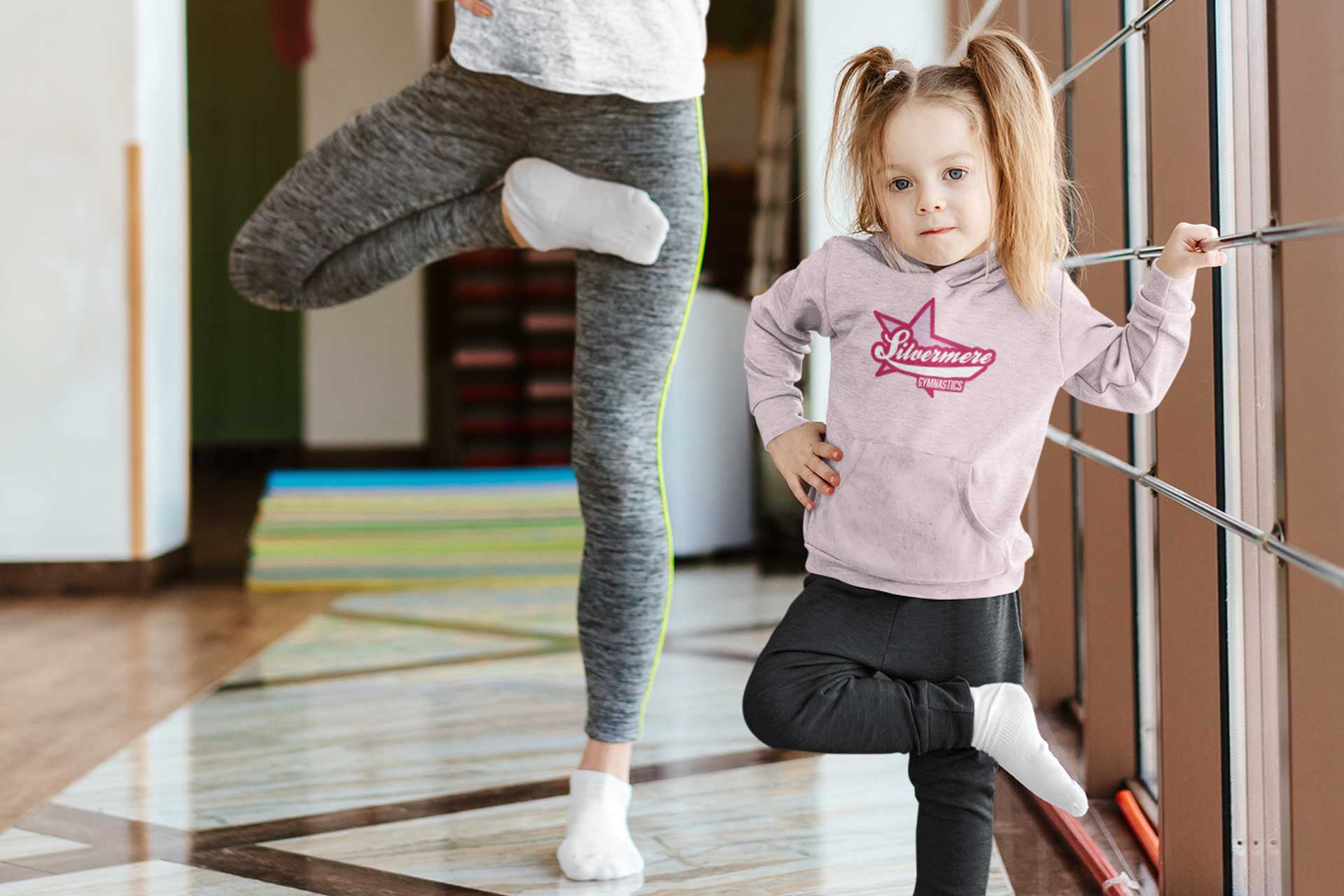 A young girl stretching and wearing a Silvermere Gymnastics Hoodie